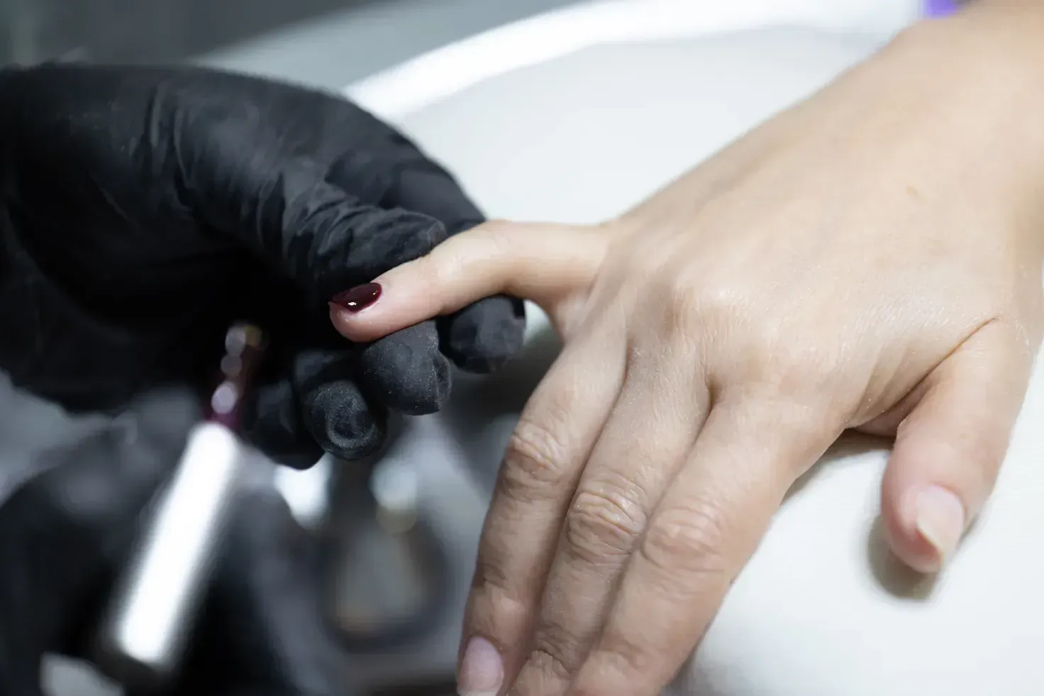 Una mujer se deja pintar las uñas por un artista que lleva guantes negros.