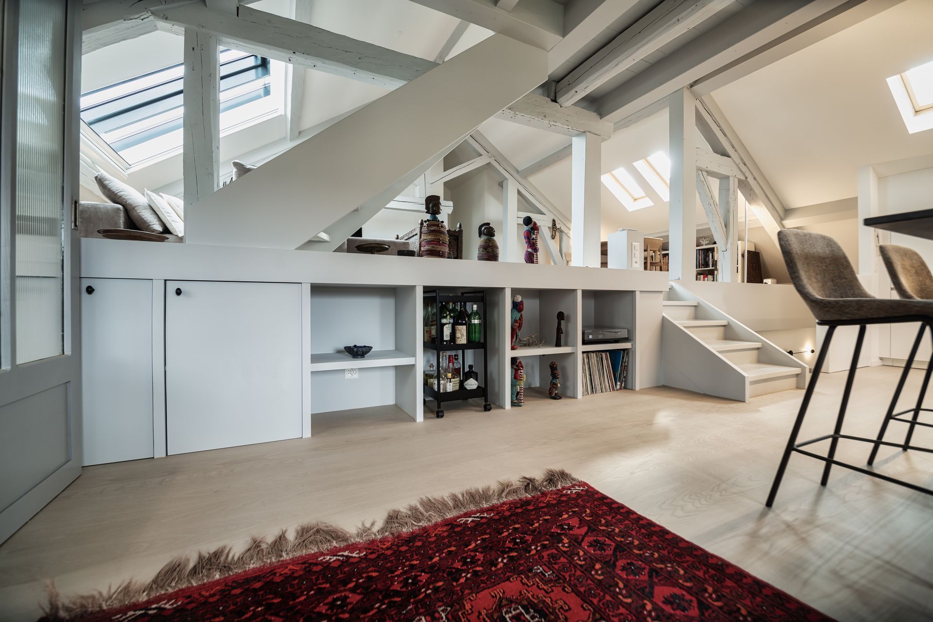 A living room with stairs leading up to the second floor and a rug on the floor.