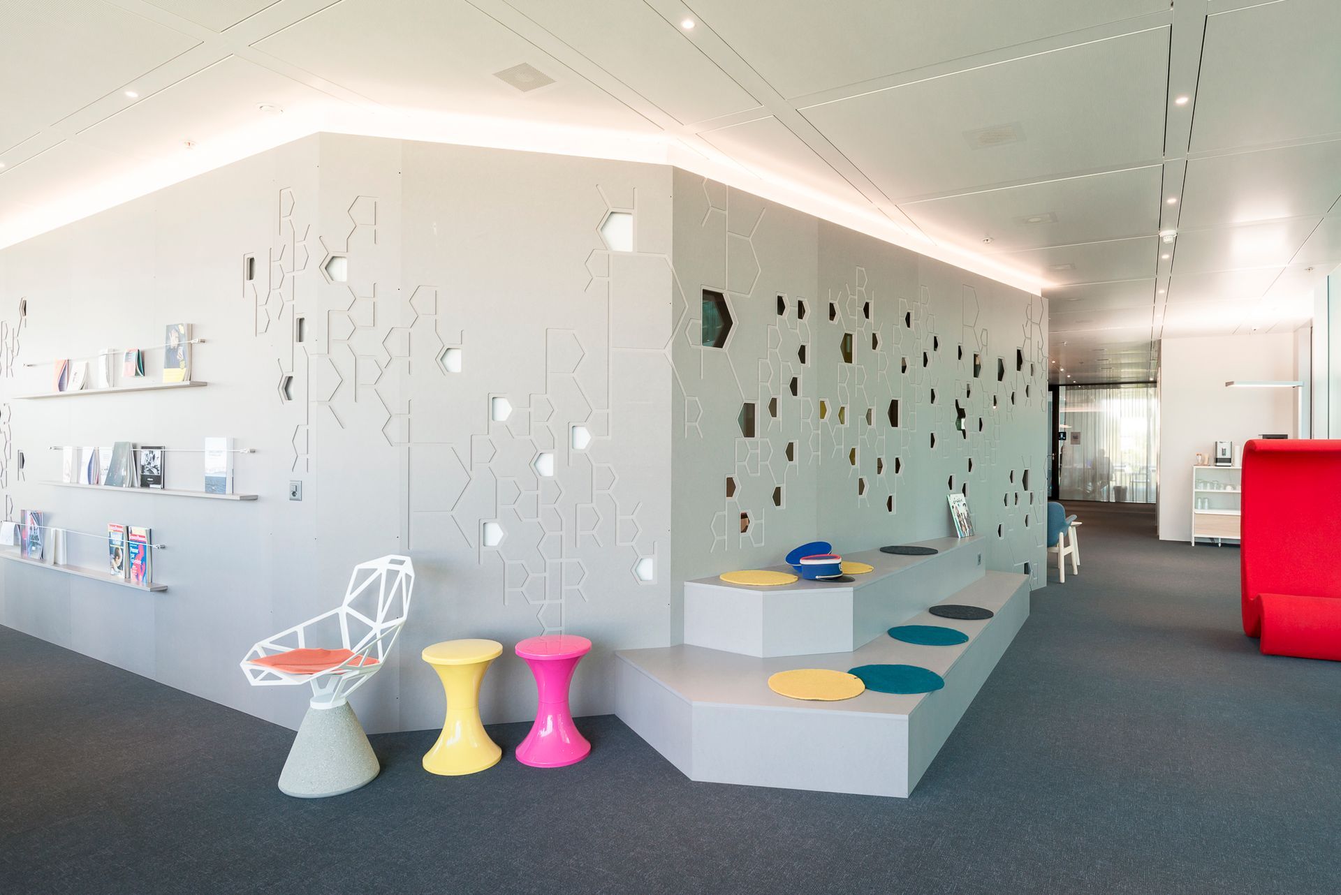 A room with a staircase , chairs , stools and a red chair.