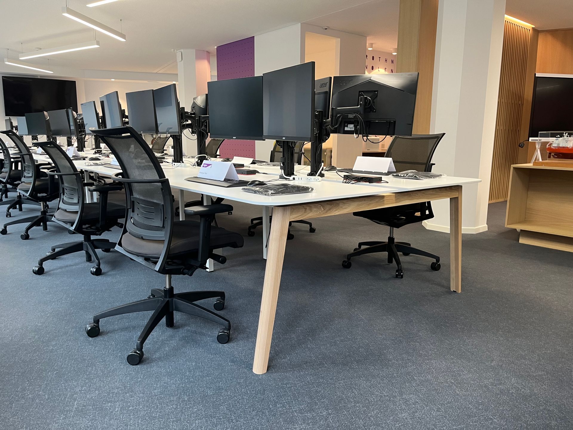 A row of desks with computers and chairs in an office.