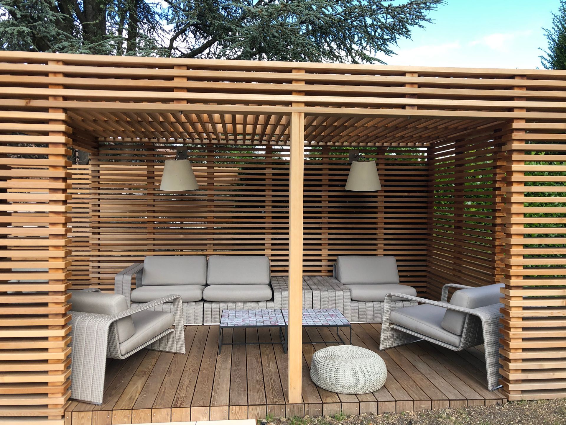 A wooden gazebo with a couch , chairs , and a table.