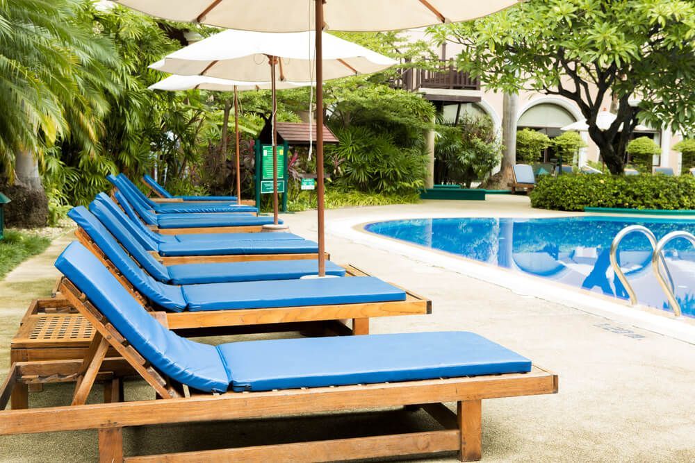Scène au bord de la piscine avec des chaises longues bleues, des parasols blancs et une piscine bleue.