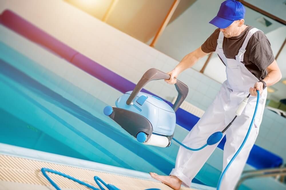 Un agent d'entretien de piscine tient un aspirateur robotisé au bord d'une piscine.