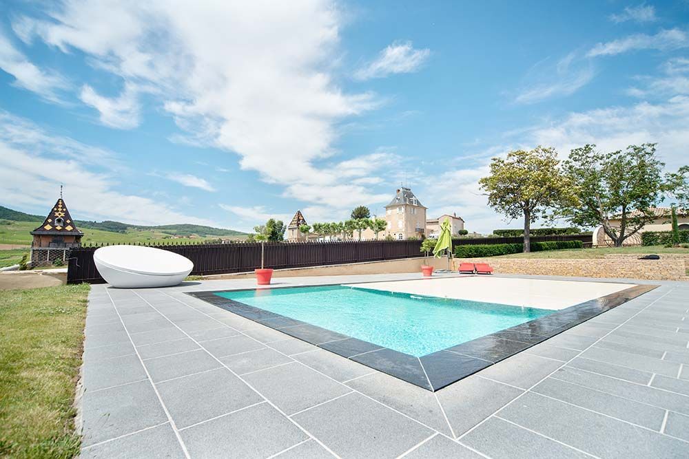 Piscine extérieure donnant sur une pelouse, un château et un ciel nuageux.
