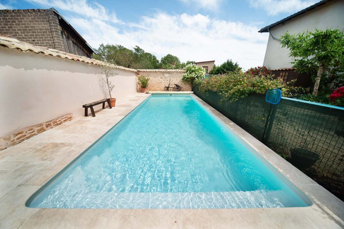Piscine rectangulaire turquoise entourée d'une terrasse en pierre claire.