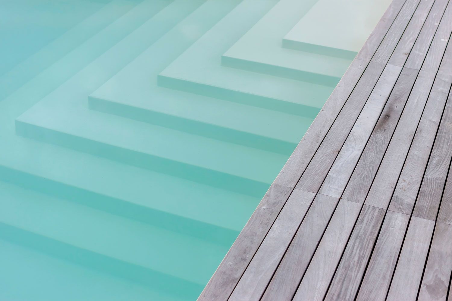 Piscine avec accès par gradins et terrasse en bois. Eau turquoise, bois clair.