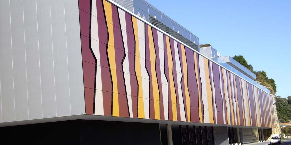 Mural de rayas coloridas en el lateral de un edificio moderno bajo un cielo azul.