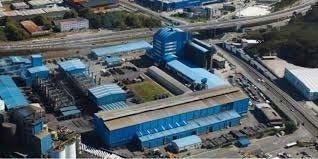 Vista aérea de un complejo industrial con techo azul junto a carreteras y vías férreas.