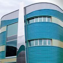 Fachada de edificio moderno con paneles curvos de color turquesa y detalles verticales blancos.