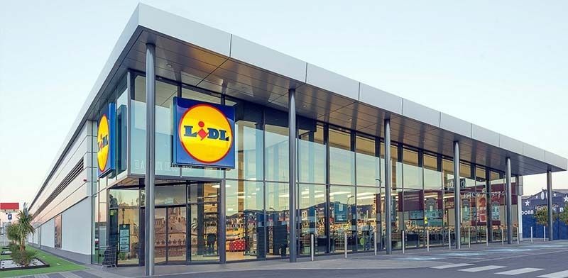 Fachada moderna de un supermercado Lidl con grandes ventanales y logotipo amarillo y azul.