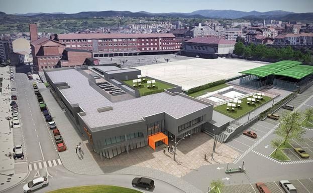 Vista aérea de un gran edificio moderno con techo gris, entrada naranja y una plaza en un paisaje urbano.