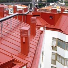 Techos de metal rojo con chimeneas en un edificio con vistas a un paisaje urbano.