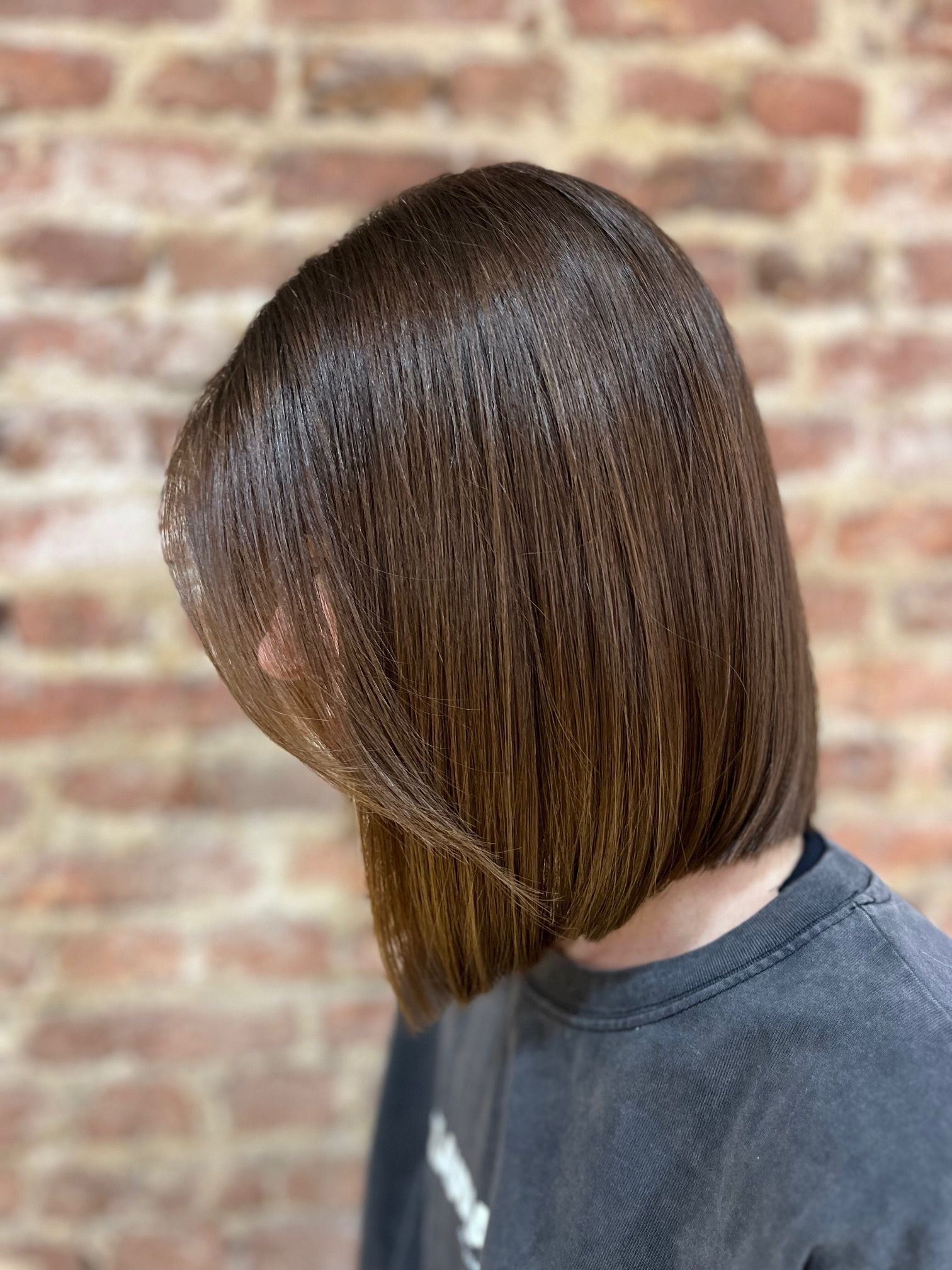 Una mujer con cabello corto y castaño viste un suéter negro y está parada frente a una pared de ladrillos.