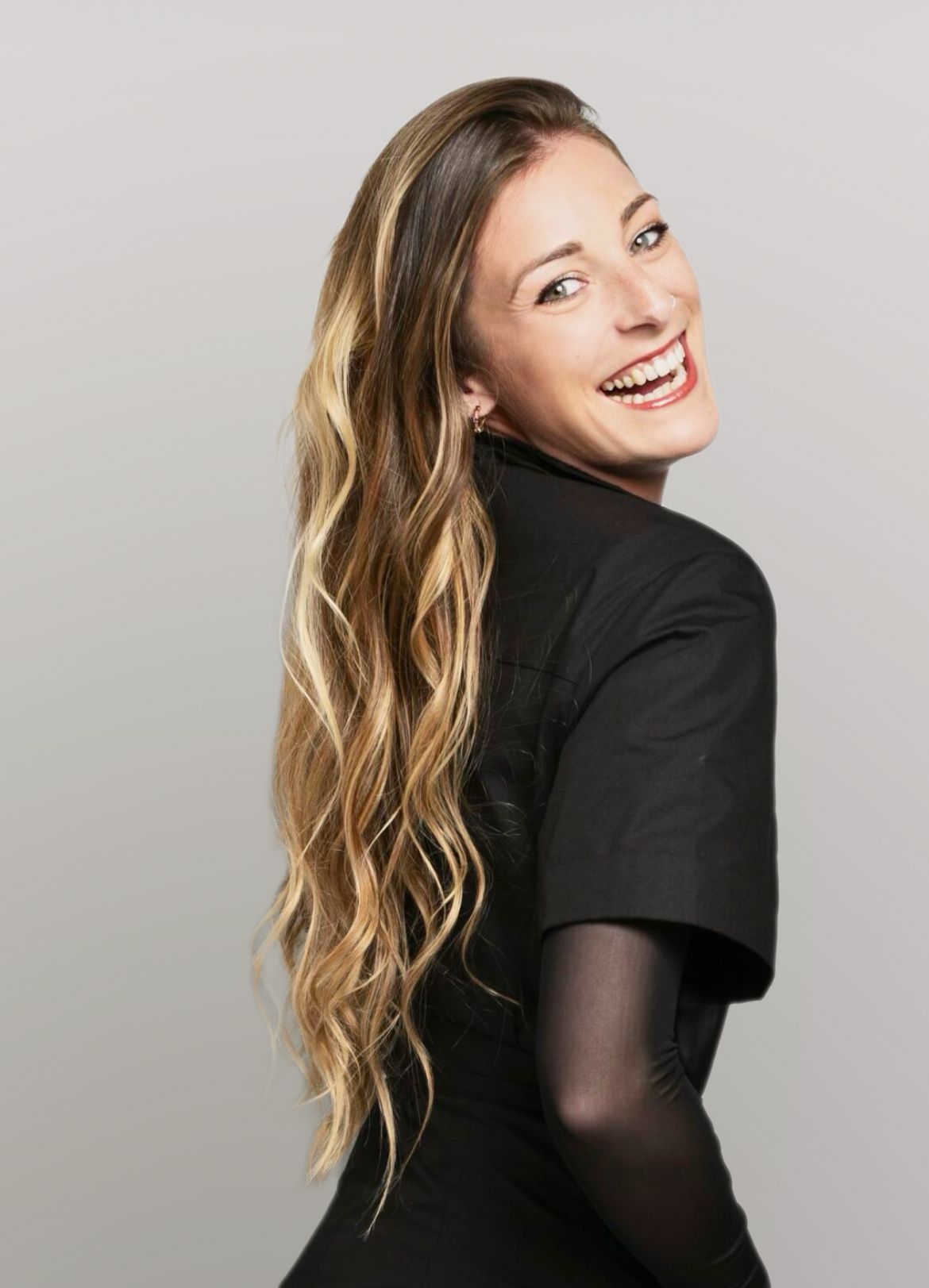 Una mujer con cabello largo y rubio lleva un vestido negro y sonríe.