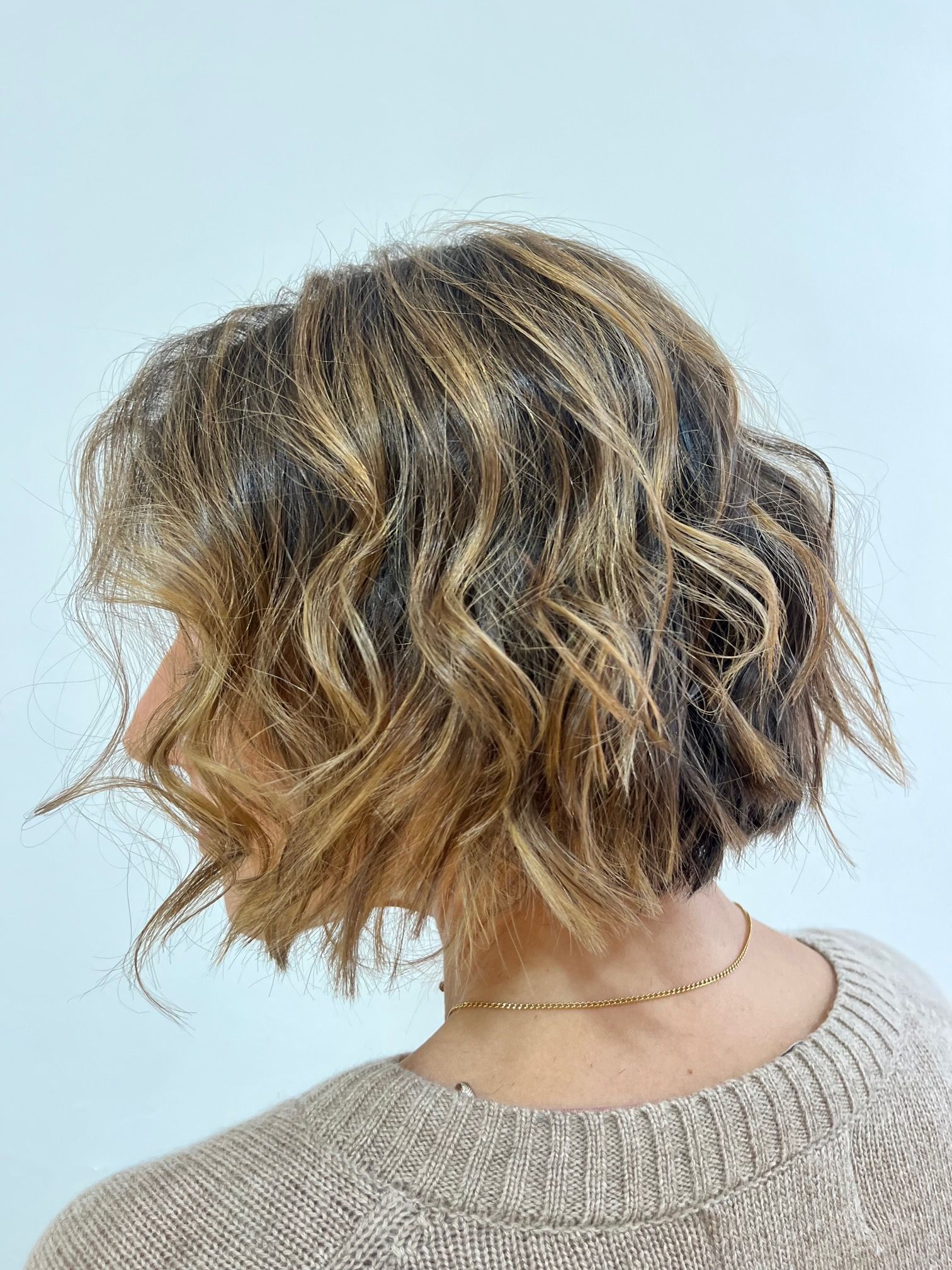 Una mujer con cabello corto y ondulado lleva un suéter y un collar.