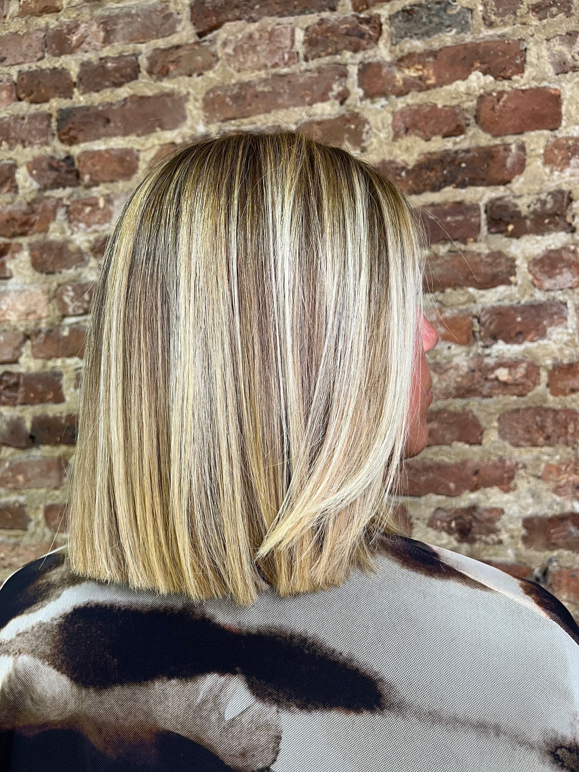 Una mujer con cabello rubio está parada frente a una pared de ladrillos.