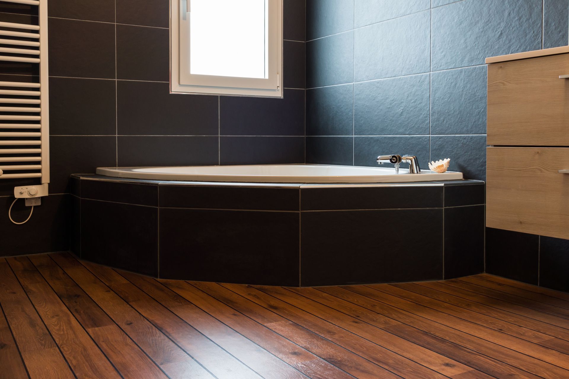 Salle de bains avec murs carrelés foncés, parquet et baignoire blanche.