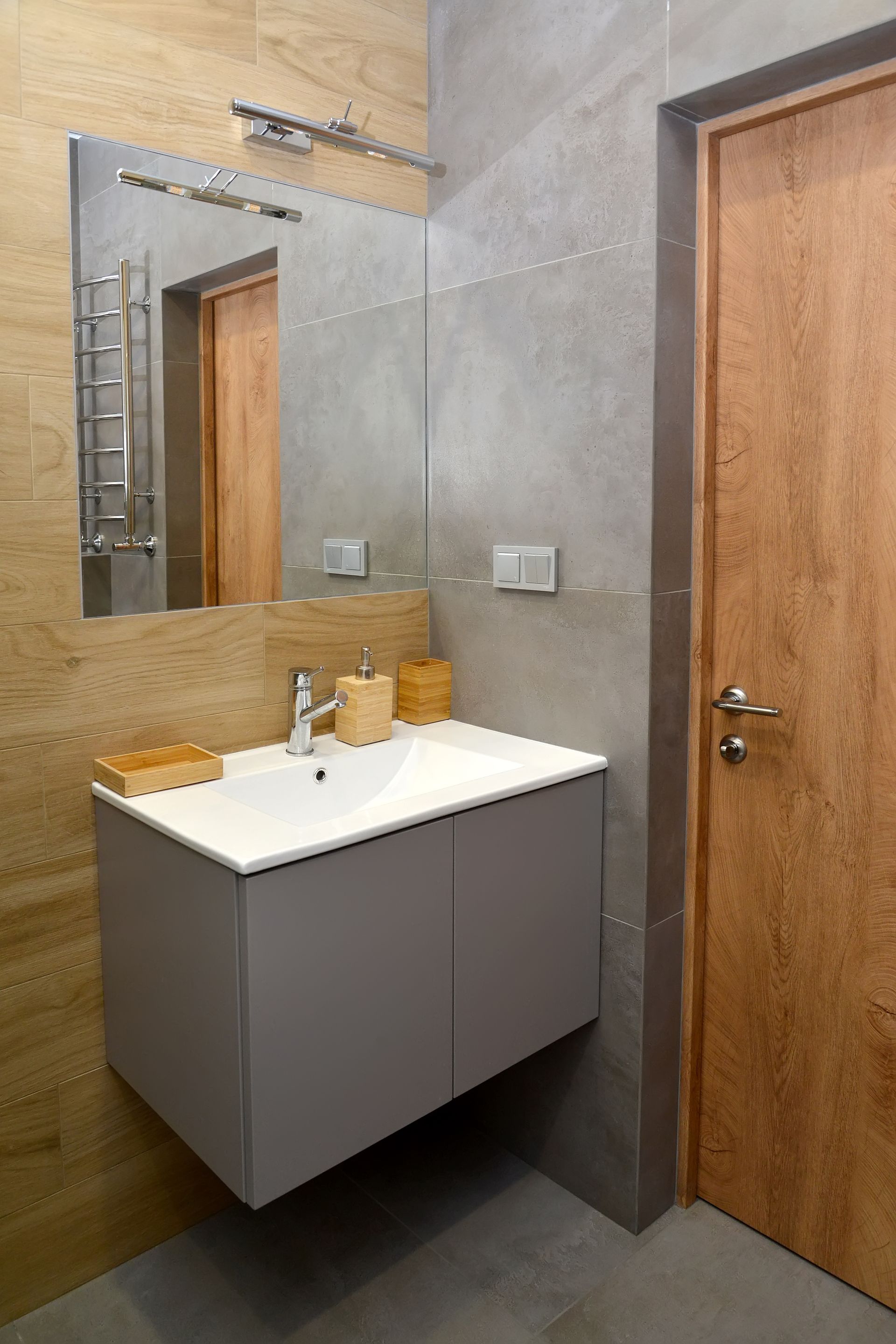 Salle de bains moderne avec meuble-lavabo gris suspendu, grand miroir et porte couleur bois.