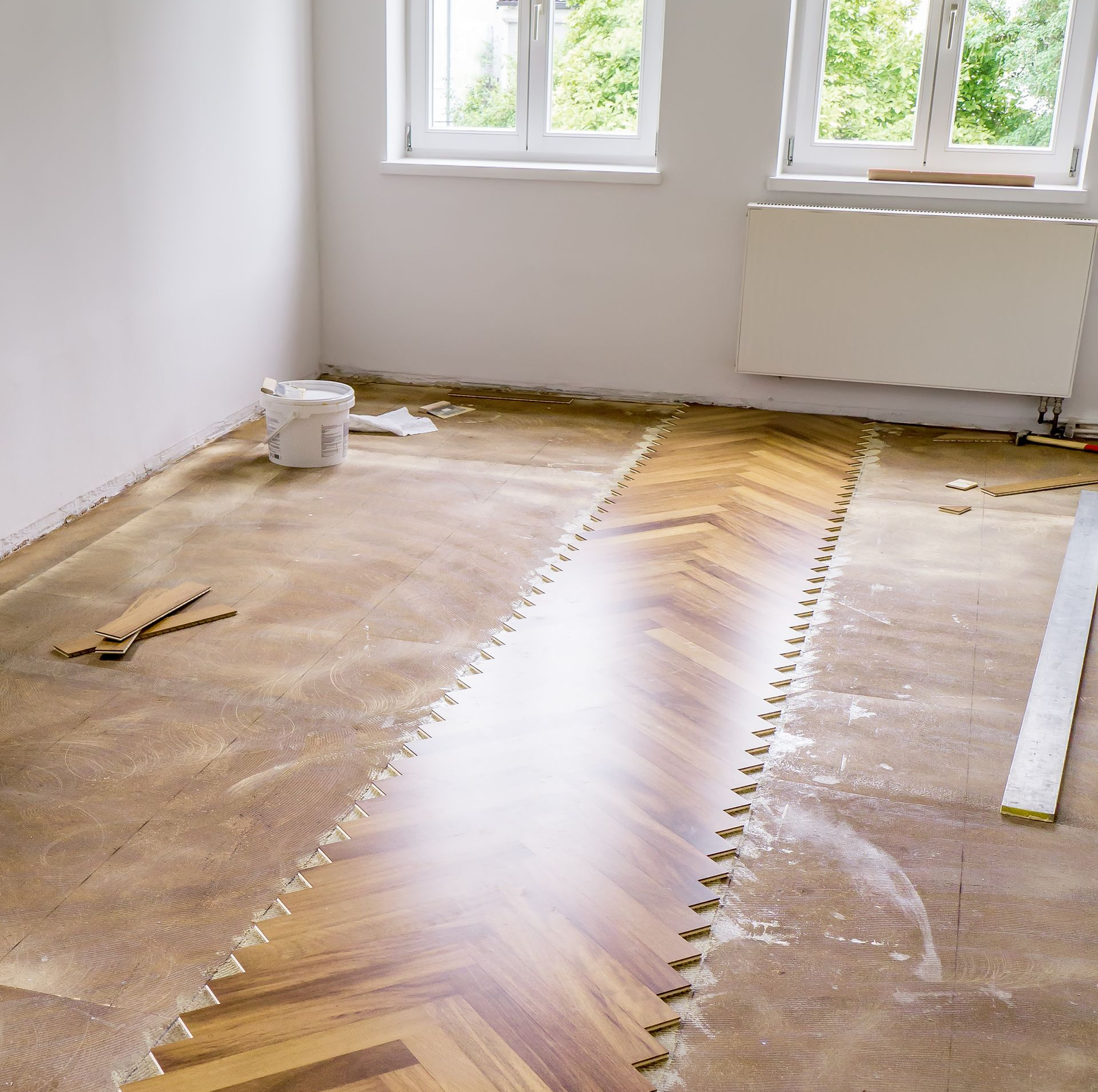 Pièce avec pose de parquet en cours ; travaux partiellement terminés, outils et matériaux visibles.