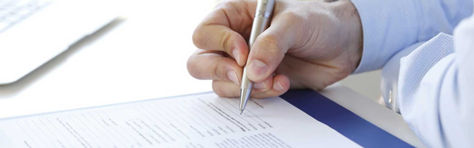 Eine Person schreibt mit einem Stift auf ein Blatt Papier.