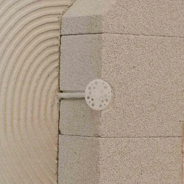 Primer plano de un sujetador de plástico blanco que asegura bloques de construcción en capas de color gris claro en una esquina.