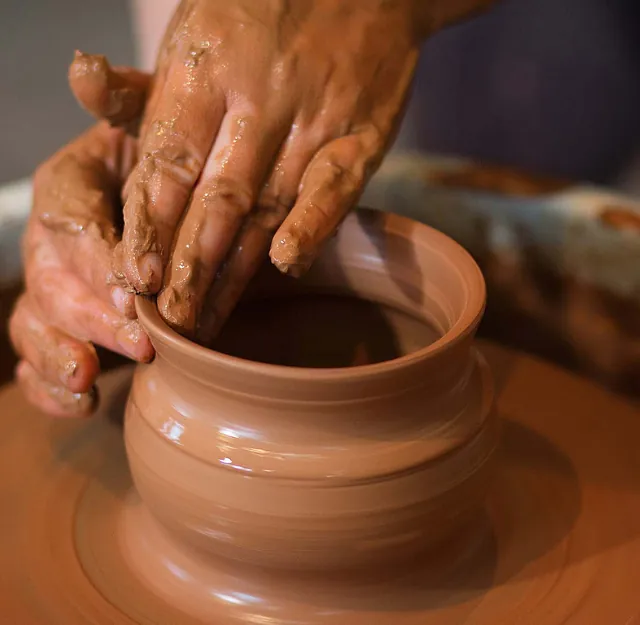 Manos dando forma a una olla de barro húmedo en un torno de alfarero; arcilla marrón, en el interior.
