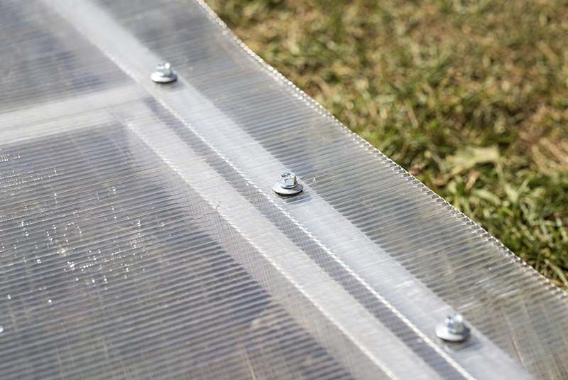 Primer plano de paneles de plástico transparente corrugado fijados con tornillos metálicos sobre una superficie cubierta de césped.
