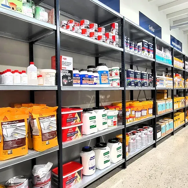 Estantes llenos de materiales de construcción en una tienda, incluidas latas de pintura, baldes y bolsas.