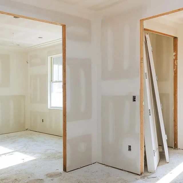 Habitación interior en construcción; paredes de yeso, marcos de puertas de madera y puertas sin instalar.