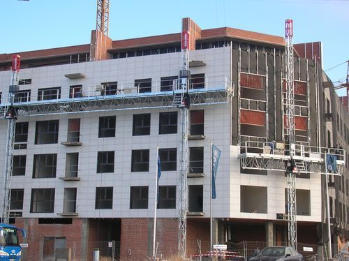 Sitio de construcción, edificio de varios pisos con andamios; exterior blanco y marrón.