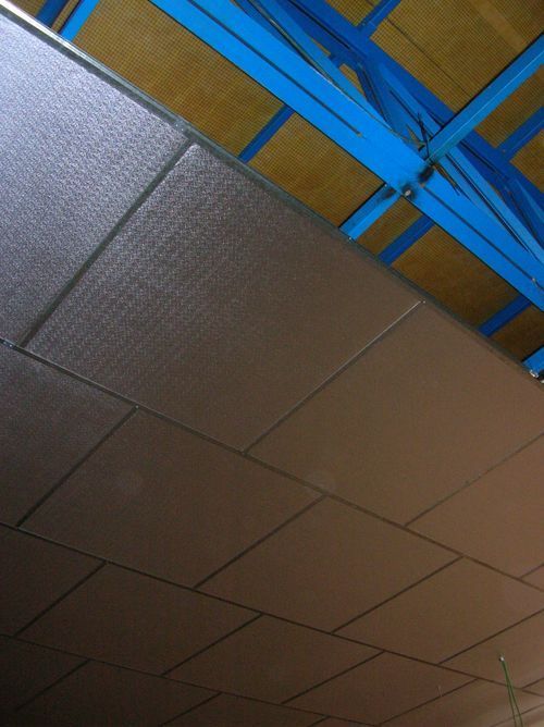 Primer plano de un techo revestido con paneles rectangulares de color marrón, sostenidos por vigas metálicas de color azul.