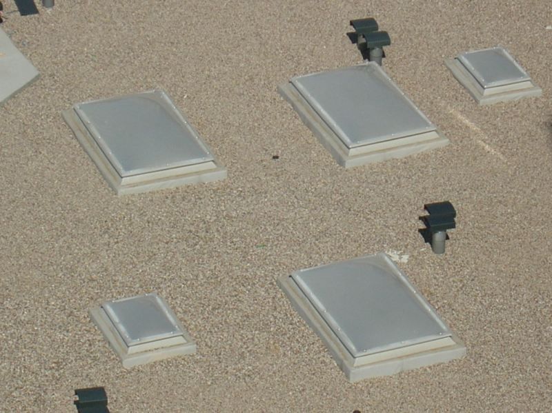 Claraboyas en un tejado plano de grava. Gris y blanco, con soportes de montaje negros.