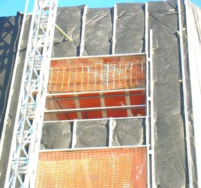 Exterior de una obra en construcción con lona negra, malla naranja y un andamio plateado.