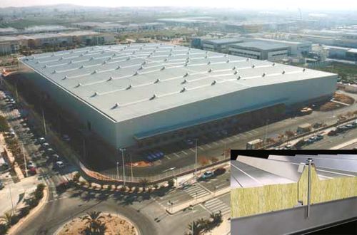 Gran edificio industrial con techo de metal de color claro; el recuadro muestra el aislamiento del techo con material amarillo.