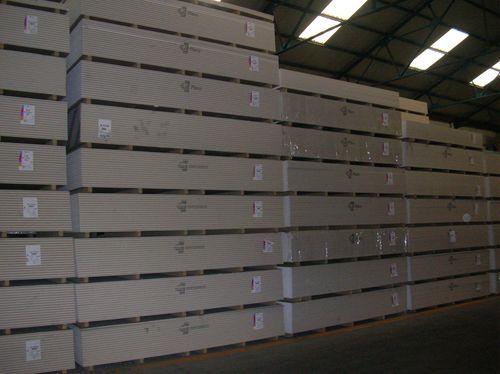Pilas de láminas de yeso envueltas en plástico, almacenadas en un almacén.