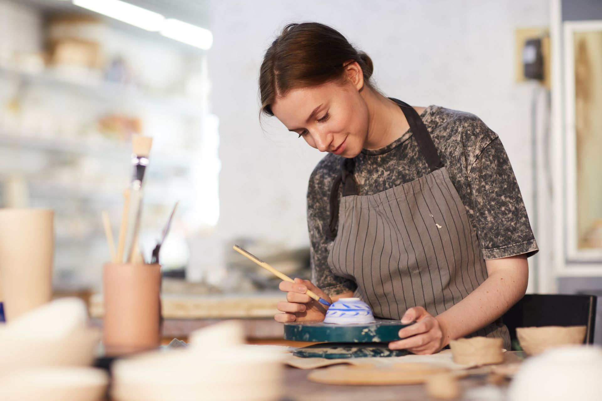 Mujer pintando un cuenco de cerámica, con delantal, en un taller de cerámica.