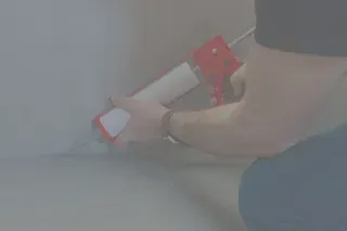 Persona calafateando una costura de esquina con una pistola de calafateo roja y blanca.