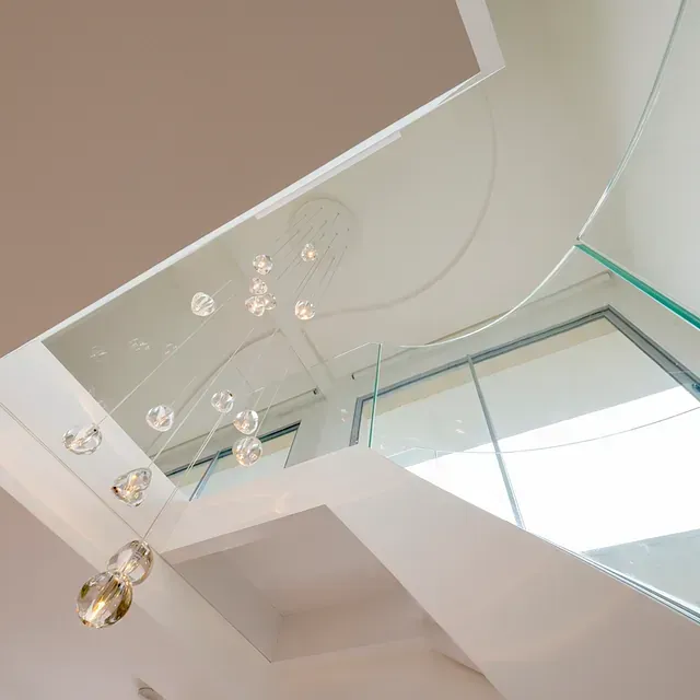 Escalera interior moderna con barandilla de cristal y luminaria decorativa.