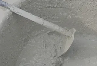 Una paleta mezcla cemento gris claro en un balde.