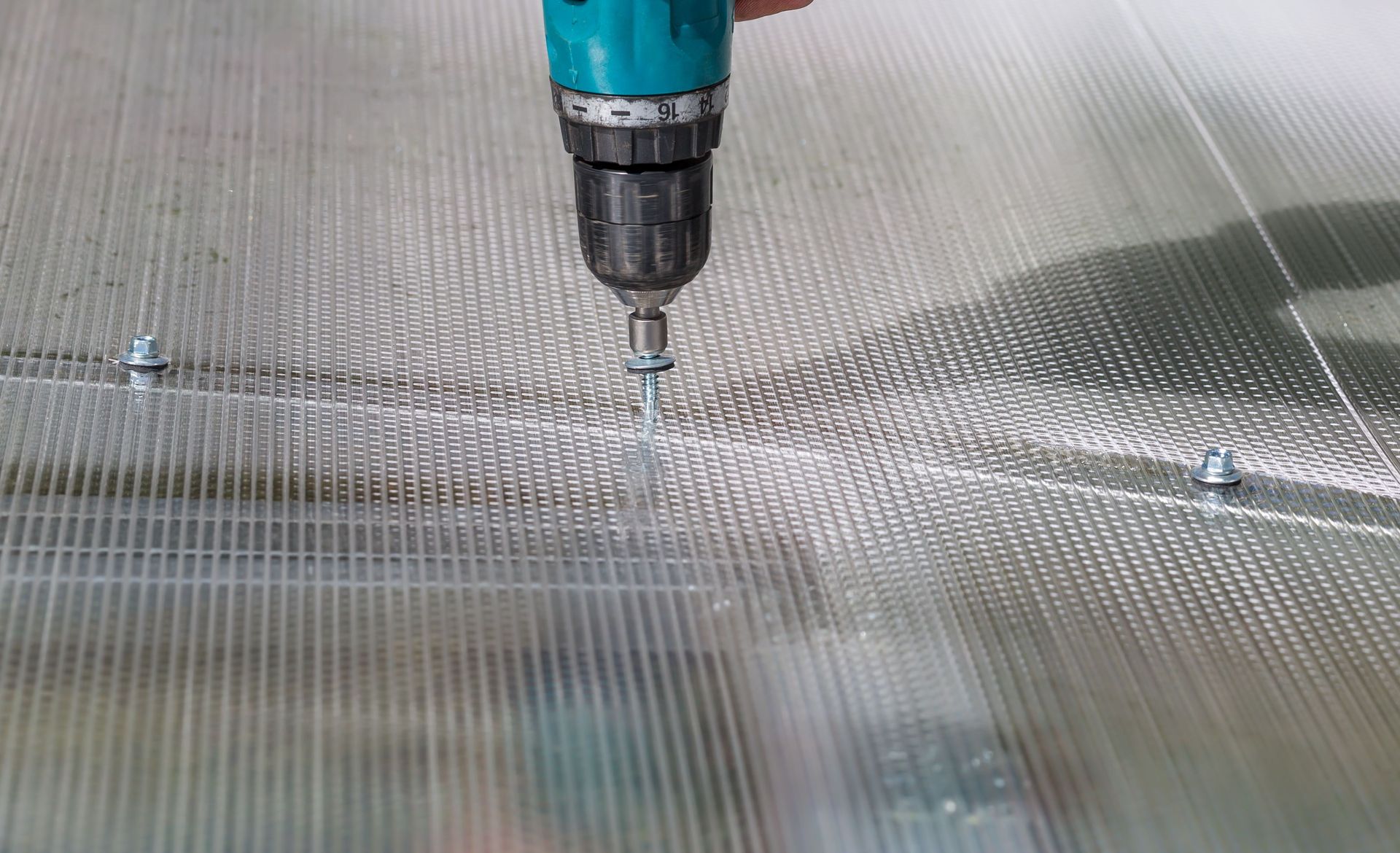 Una persona que utiliza un taladro para fijar tornillos a un panel de plástico corrugado.