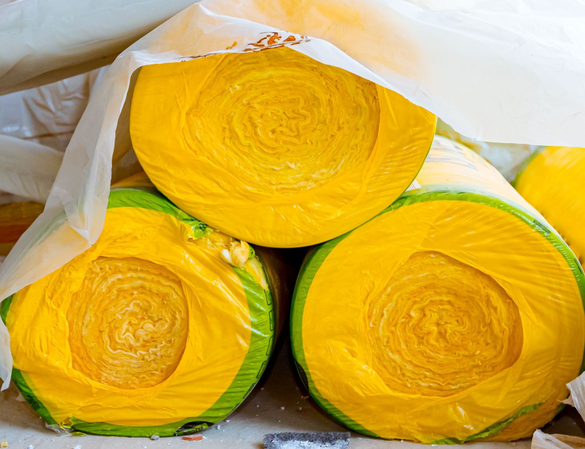 Rollos amarillos de aislamiento envueltos en plástico, apilados bajo una lona transparente.