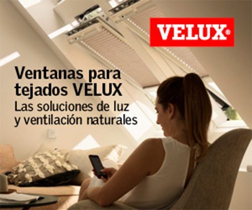 Mujer usando el teléfono bajo las ventanas de techo VELUX. Interior moderno y luminoso con luz natural.
