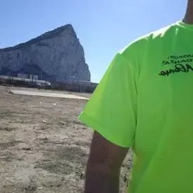 Un hombre con una camiseta verde neón está parado frente a una montaña.