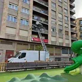 Una camioneta blanca está estacionada frente a un edificio al lado de un tobogán verde.