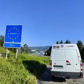 Una camioneta blanca está estacionada al costado de la carretera al lado de un cartel azul.