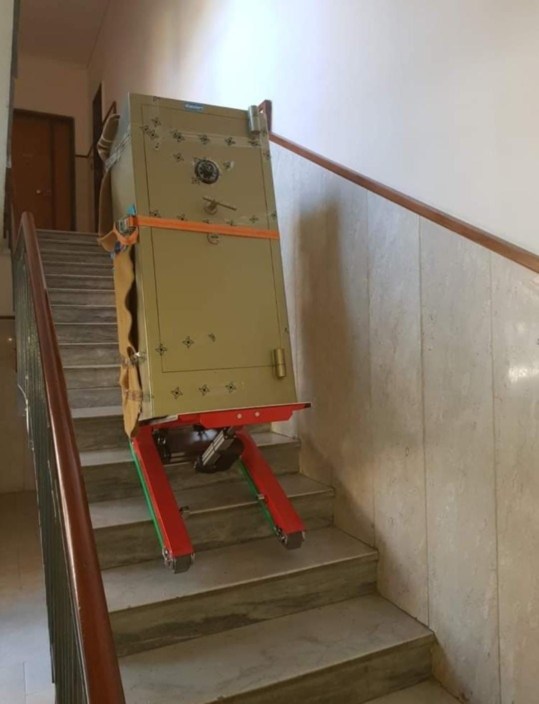 Se está subiendo una caja fuerte por unas escaleras sobre una plataforma rodante.