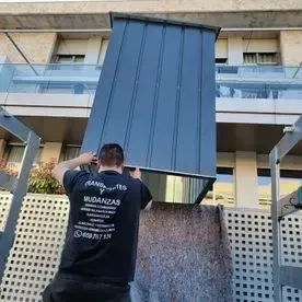 Un hombre lleva un gran trozo de metal delante de un edificio.