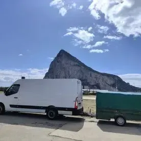 Una camioneta blanca remolca un remolque verde con una montaña al fondo.
