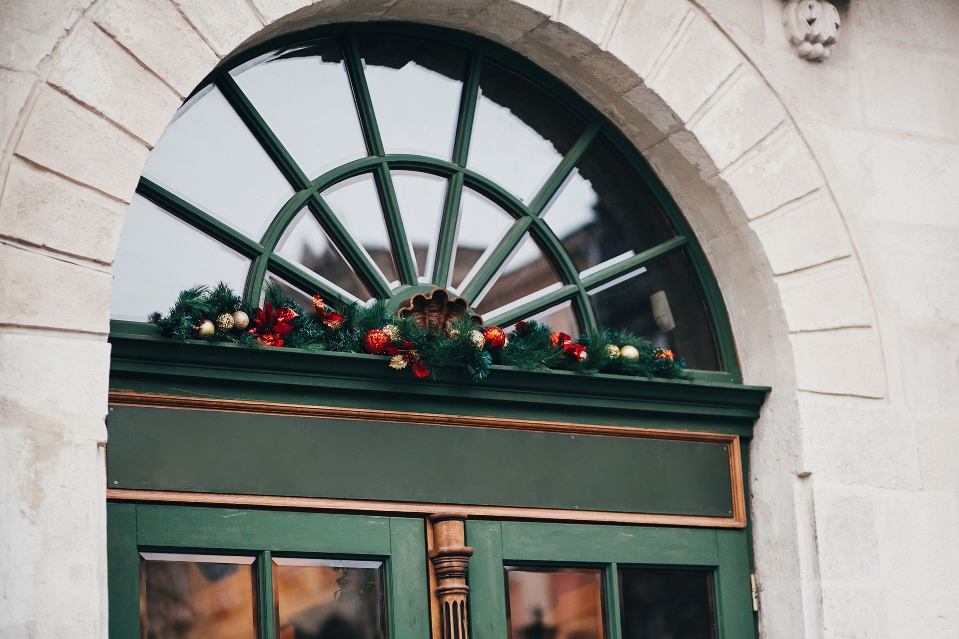 Una puerta verde con una ventana circular y adornos navideños.