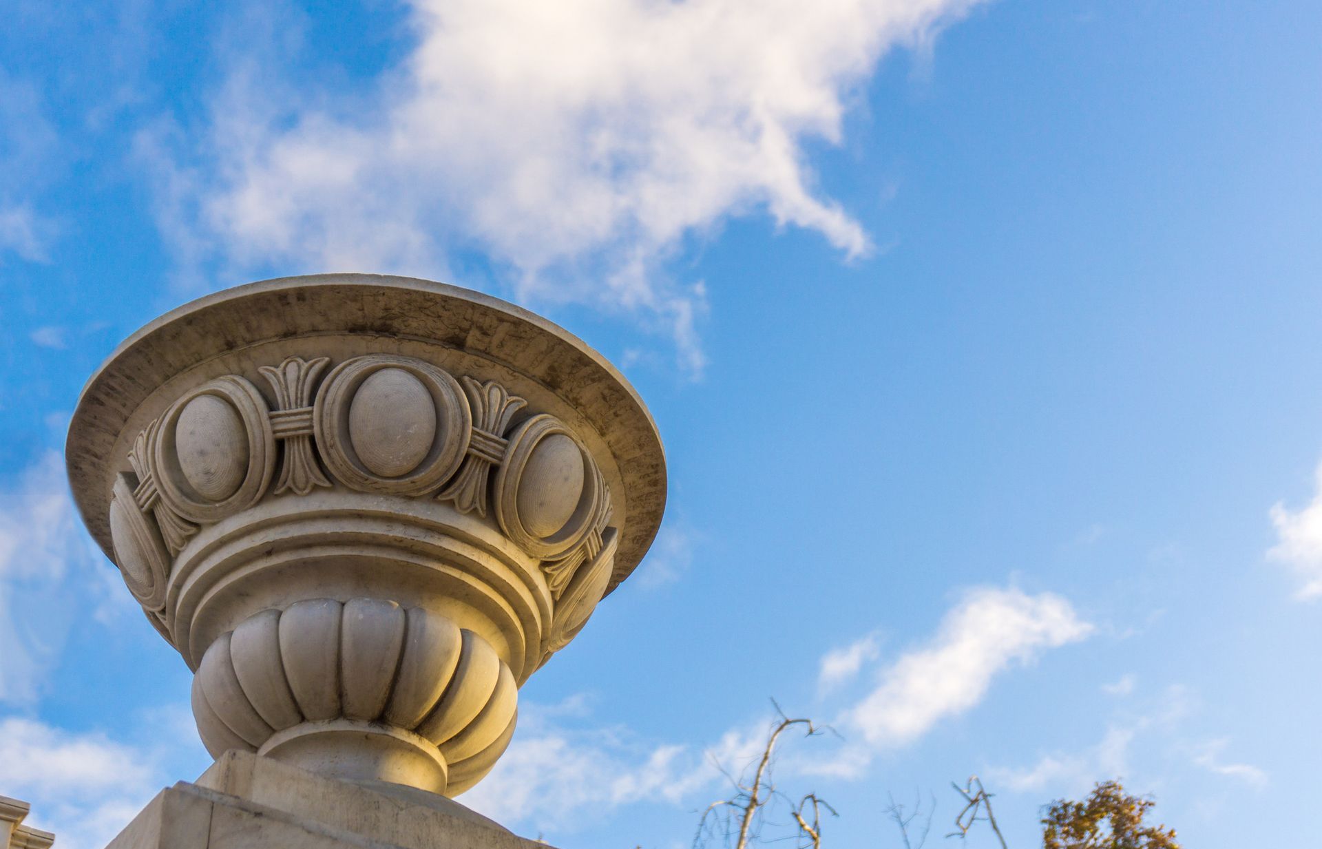 Una estatua de un jarrón contra un cielo azul con nubes.
